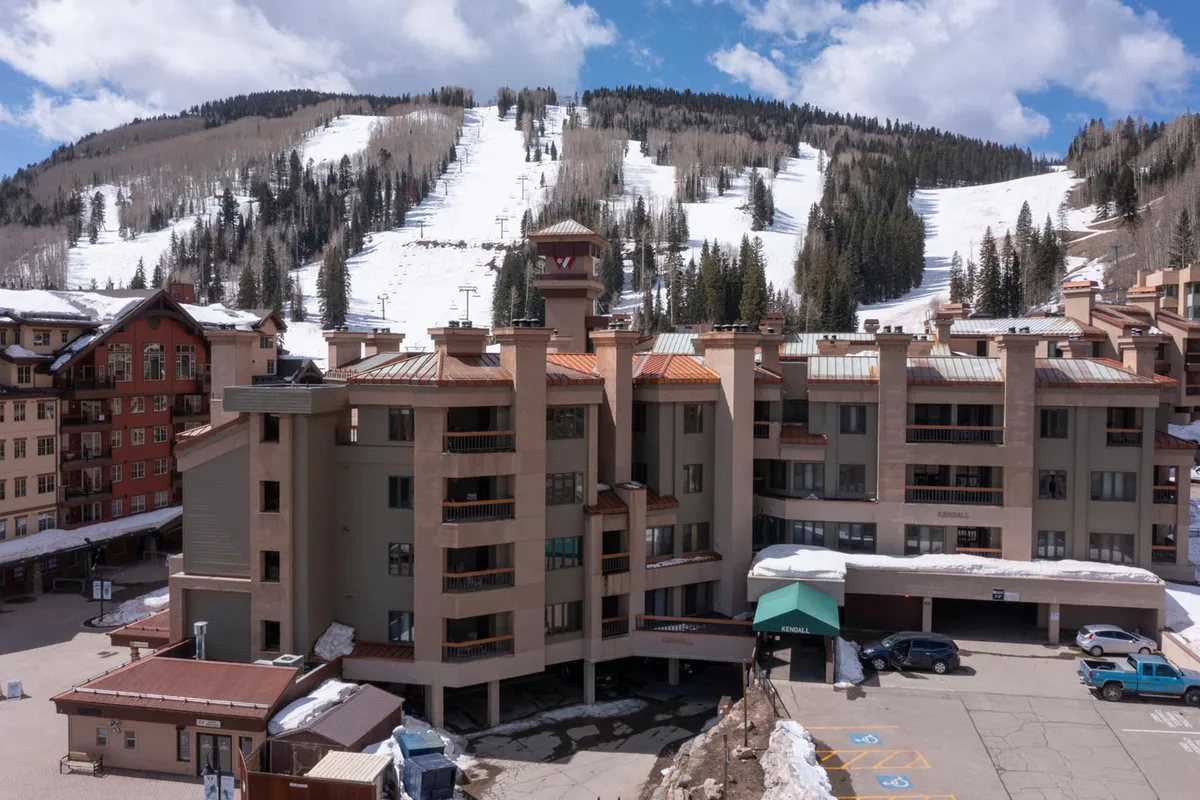 A scenic exterior view of the resort building, surrounded by snow-covered slopes and tall pine trees. The architecture stands out against the serene mountain backdrop, illustrating the property's proximity to both adventure and nature.