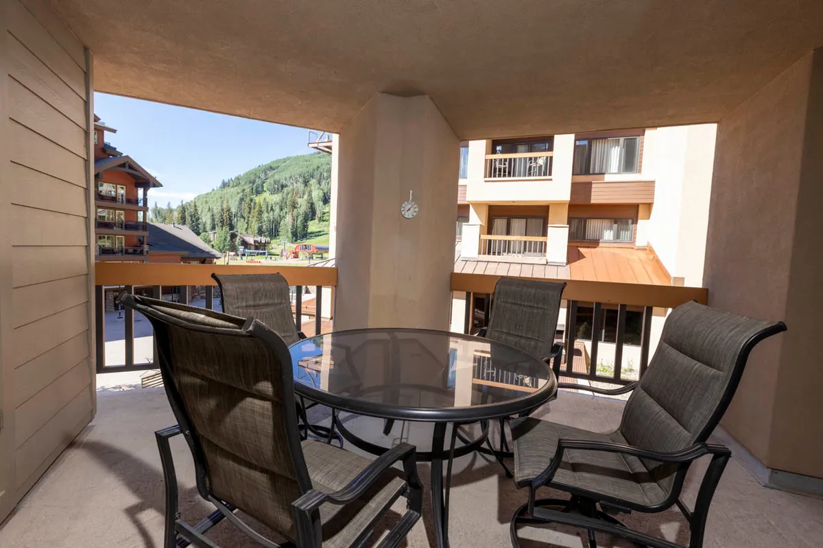 This image showcases an inviting outdoor patio featuring a table and chairs, framed by a scenic mountain view in the background. The setup suggests a comfortable spot for families to gather for meals, enjoy morning coffee, or simply relax while taking in the natural surroundings.