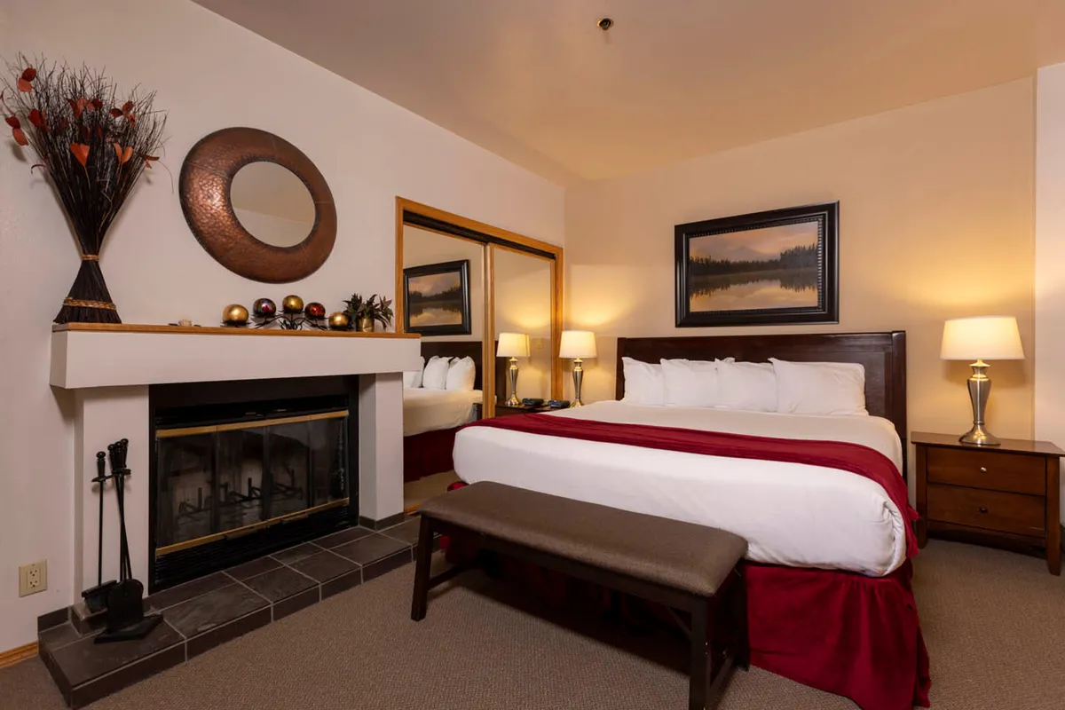 This image highlights a bedroom with a cozy bed, a warm fireplace, a mirror, and tasteful decorative arrangements. The space exudes warmth and quiet, suggesting restful evenings and a soothing retreat from the day.