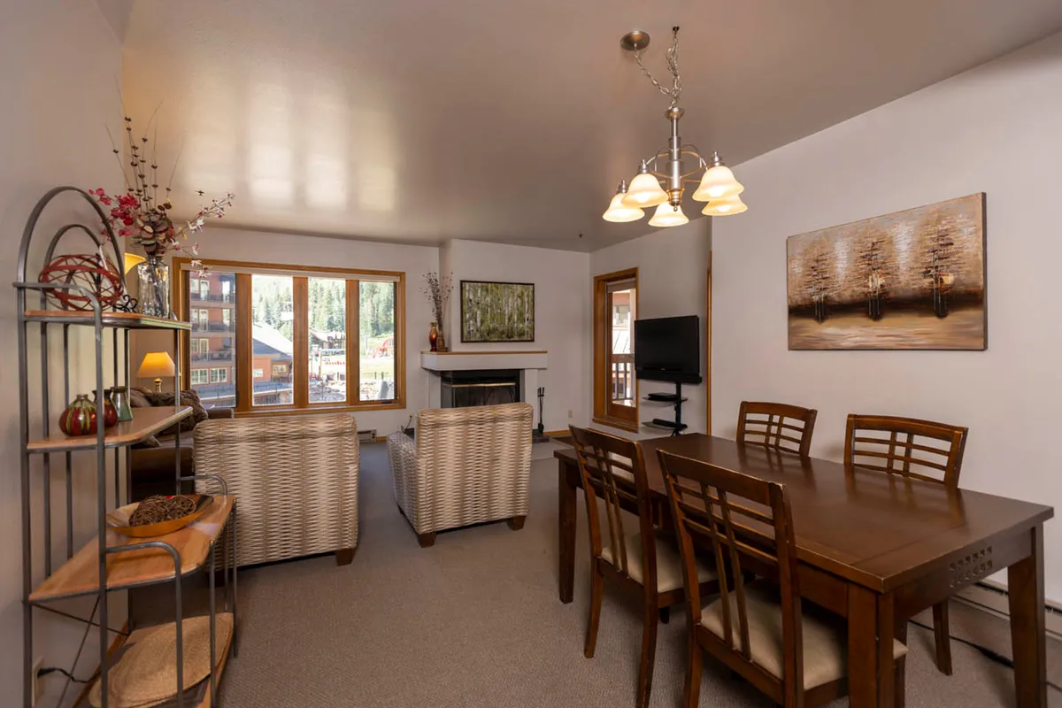 A cozy dining area with a prominent fireplace, a large table set for shared meals, and expansive windows that let in natural light. The scene is enhanced by tasteful artwork, creating a space ideal for family dinners, social gatherings, and relaxing by the fire.