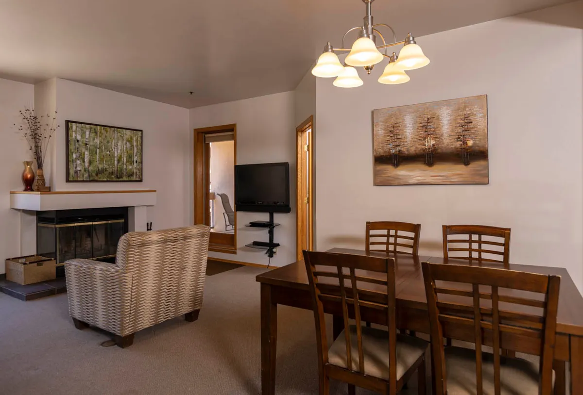 A cozy living area featuring a wood-burning fireplace, a plush armchair, and a welcoming dining table—perfect for intimate conversations, shared meals, or relaxing moments by the fire. Artwork and a television add to the inviting ambiance.